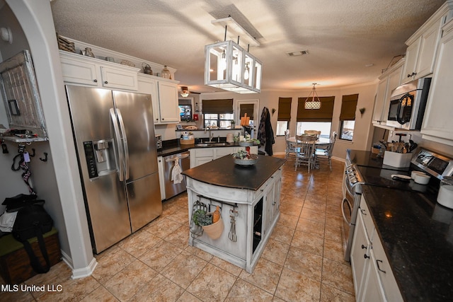 kitchen with decorative light fixtures, a textured ceiling, white cabinets, crown molding, and appliances with stainless steel finishes