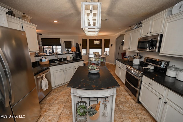 kitchen with a textured ceiling, stainless steel appliances, a kitchen island, white cabinetry, and sink