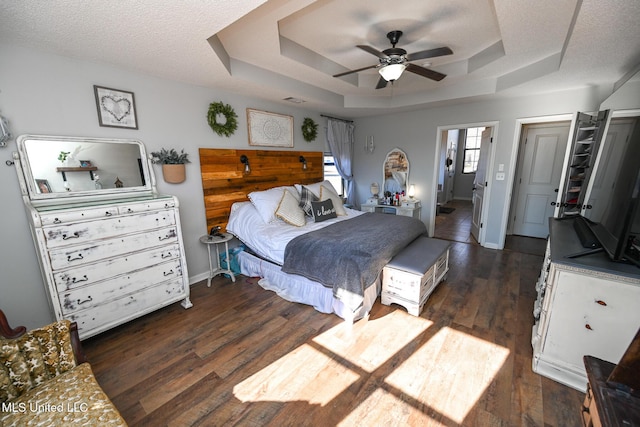 bedroom with a textured ceiling, ceiling fan, a tray ceiling, and dark hardwood / wood-style flooring