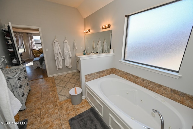 bathroom with a healthy amount of sunlight, a tub to relax in, lofted ceiling, and vanity