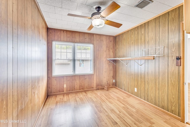 empty room with wood walls, wood-type flooring, and ceiling fan