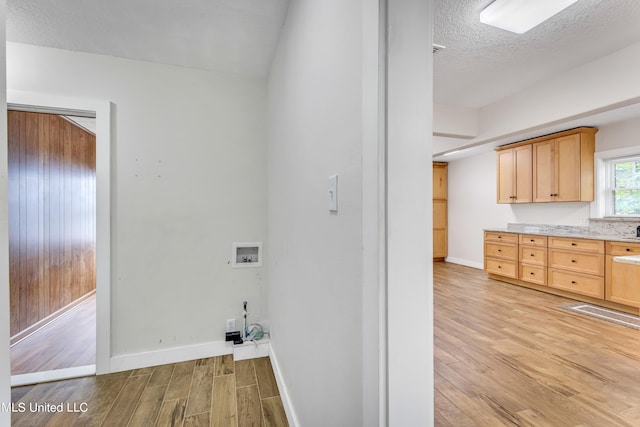 laundry area with hookup for a washing machine, a textured ceiling, light wood-type flooring, and cabinets