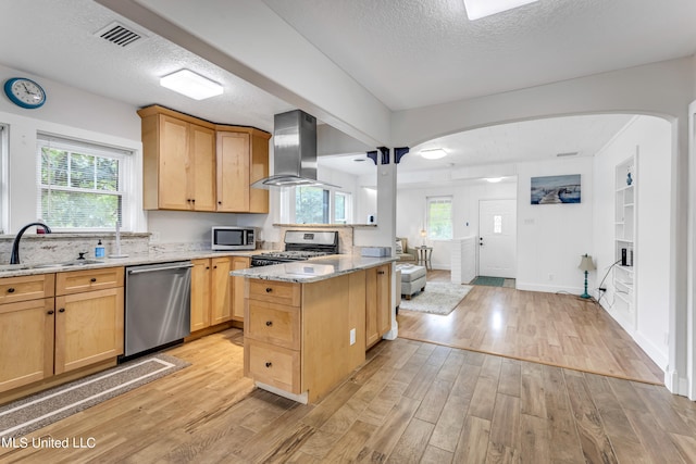 kitchen with a wealth of natural light, wall chimney range hood, stainless steel appliances, and light wood-type flooring