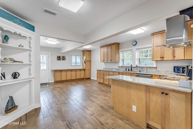 kitchen featuring wall chimney range hood, light brown cabinets, a textured ceiling, light stone countertops, and light wood-type flooring