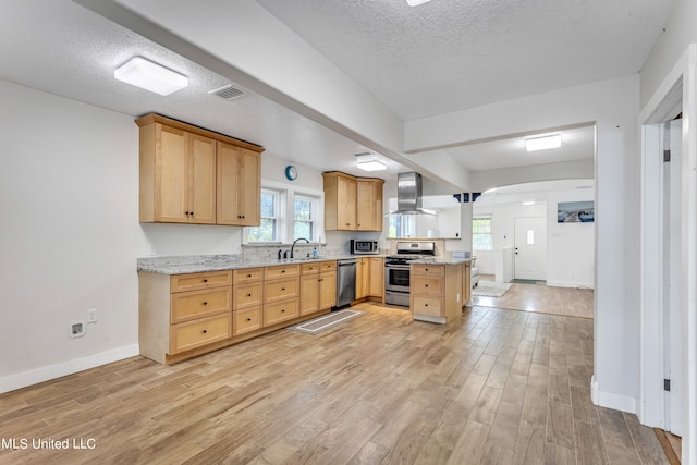 kitchen featuring wall chimney range hood, light brown cabinets, light wood-type flooring, sink, and stainless steel appliances