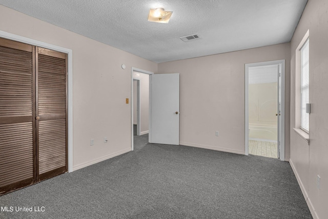 unfurnished bedroom featuring connected bathroom, dark colored carpet, a textured ceiling, and a closet