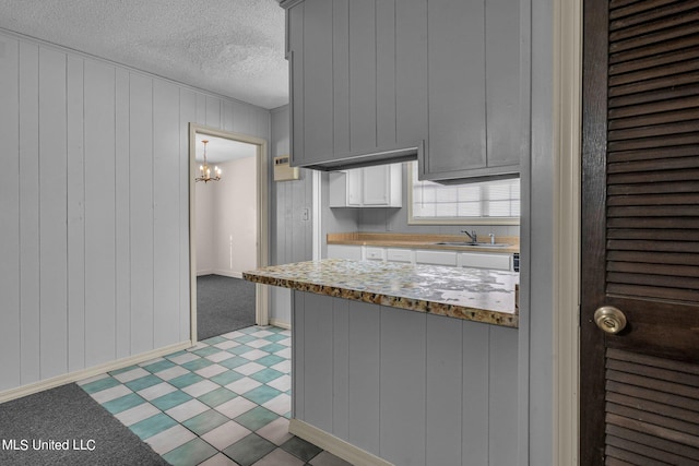 kitchen with sink, kitchen peninsula, a textured ceiling, and wooden walls