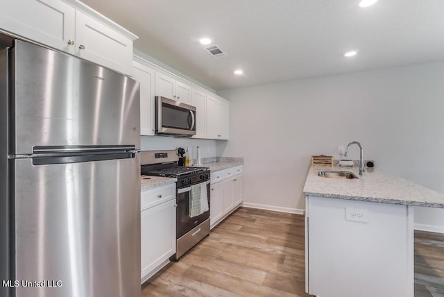 kitchen featuring a sink, stainless steel appliances, a peninsula, light wood-type flooring, and visible vents