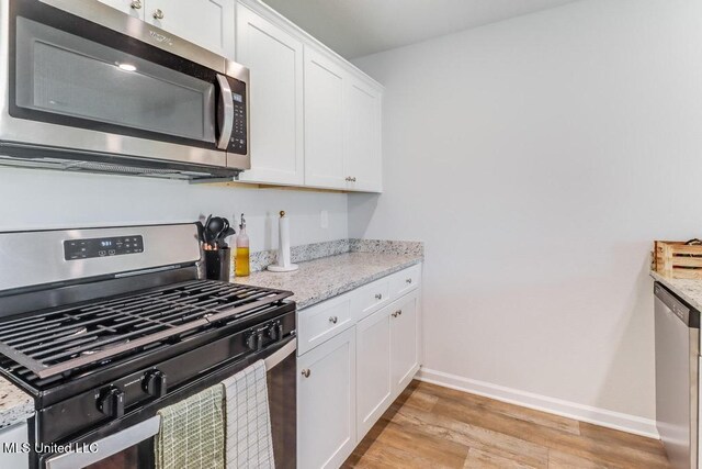 kitchen featuring appliances with stainless steel finishes, light stone counters, white cabinets, baseboards, and light wood-style flooring