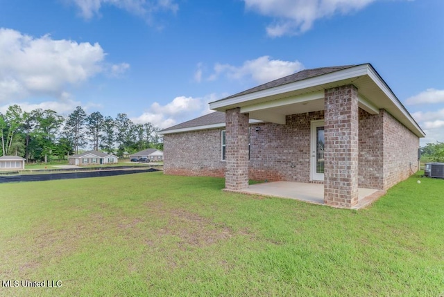 rear view of property featuring a lawn, a patio, cooling unit, and brick siding
