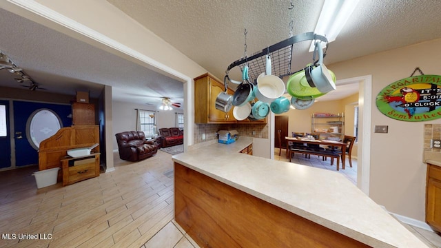 kitchen with decorative backsplash, ceiling fan, a textured ceiling, and light wood-type flooring