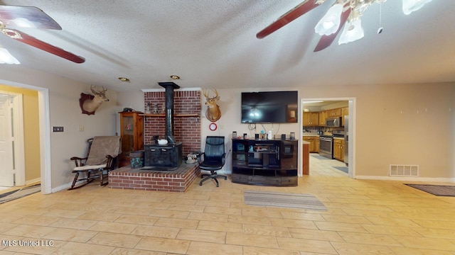 living room featuring a wood stove, ceiling fan, a textured ceiling, and light wood-type flooring