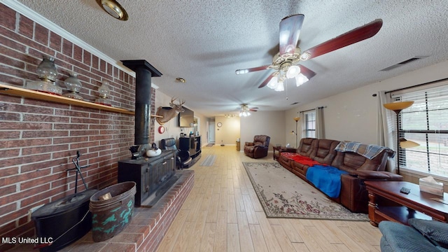 living room featuring ceiling fan, light hardwood / wood-style floors, a wood stove, and a textured ceiling