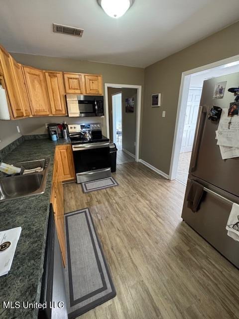 kitchen featuring dishwashing machine, sink, fridge, wood-type flooring, and stainless steel electric range oven