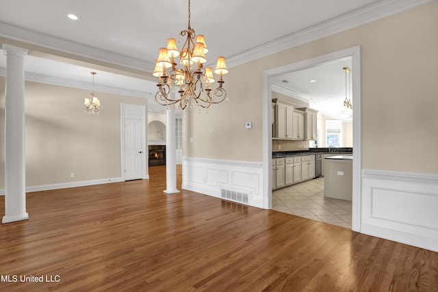 unfurnished living room with an inviting chandelier, ornamental molding, light hardwood / wood-style flooring, and decorative columns