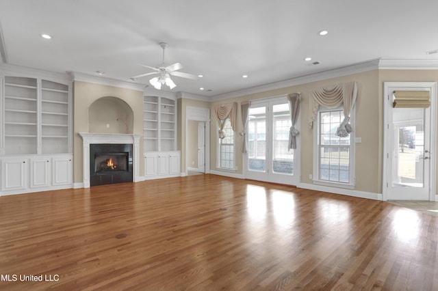 unfurnished living room featuring ceiling fan, built in features, ornamental molding, and hardwood / wood-style flooring