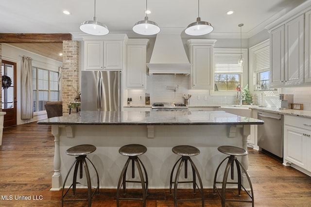 kitchen featuring stainless steel appliances, a center island, light stone countertops, custom range hood, and white cabinets