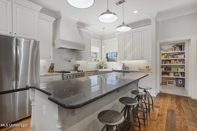 kitchen with white cabinets, stainless steel fridge, a kitchen island, custom range hood, and stove