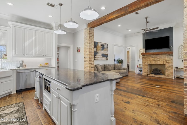 kitchen with appliances with stainless steel finishes, hanging light fixtures, white cabinets, a kitchen island, and dark stone counters