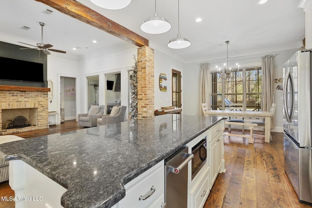 kitchen featuring pendant lighting, stainless steel refrigerator, white cabinetry, a center island, and dark stone counters