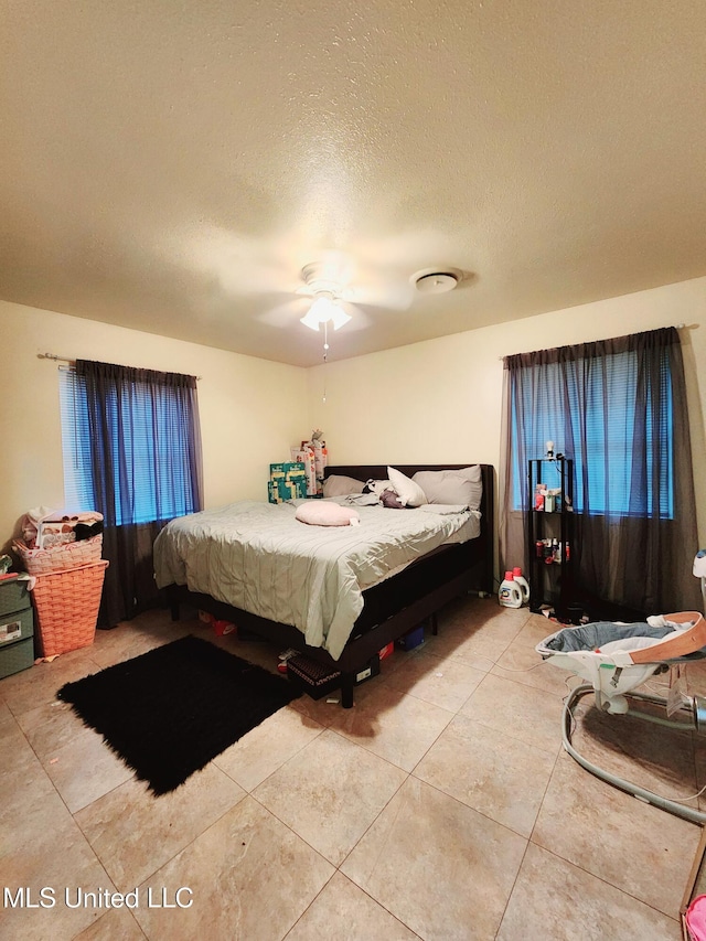 bedroom featuring ceiling fan, light tile patterned floors, and a textured ceiling