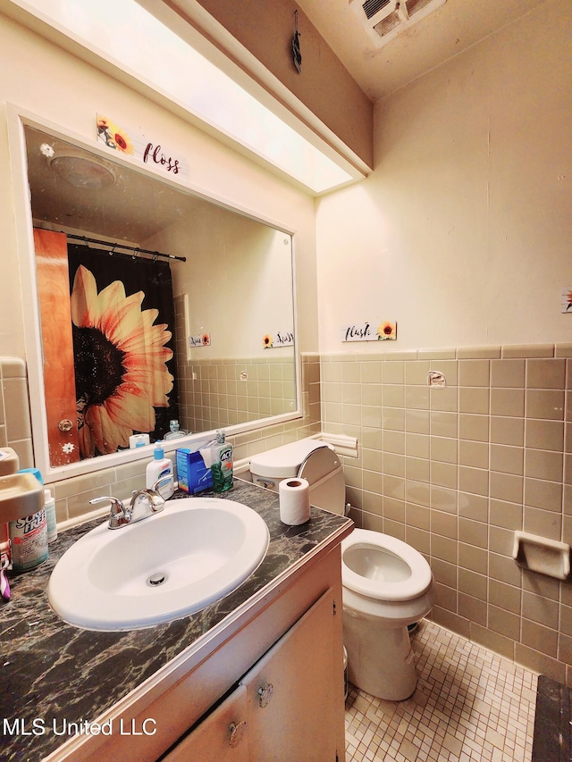 bathroom featuring tile patterned flooring, vanity, toilet, and tile walls