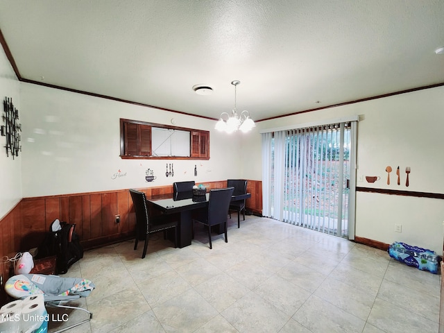 dining space with wooden walls, a chandelier, a textured ceiling, and ornamental molding