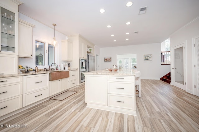 kitchen with light wood-type flooring, a center island with sink, recessed lighting, glass insert cabinets, and light stone countertops