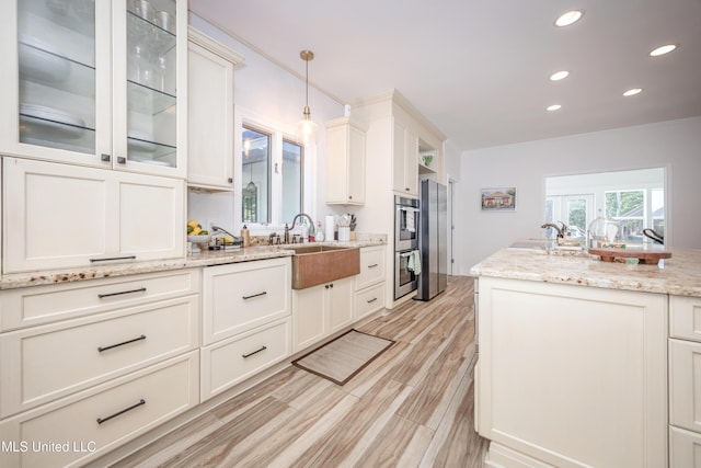 kitchen featuring hanging light fixtures, glass insert cabinets, a sink, light wood-style floors, and recessed lighting