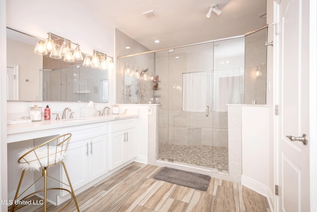 full bath with a sink, double vanity, a shower stall, and wood finished floors