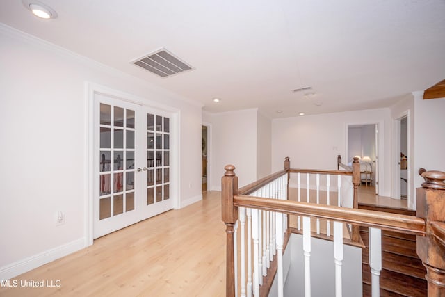 corridor featuring french doors, baseboards, visible vents, light wood-style floors, and an upstairs landing