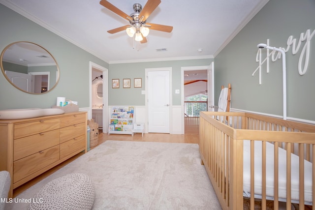 bedroom with ornamental molding, visible vents, a wainscoted wall, light wood-style floors, and a crib