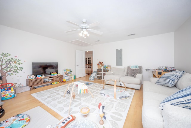 living area with wood finished floors, a ceiling fan, attic access, electric panel, and visible vents