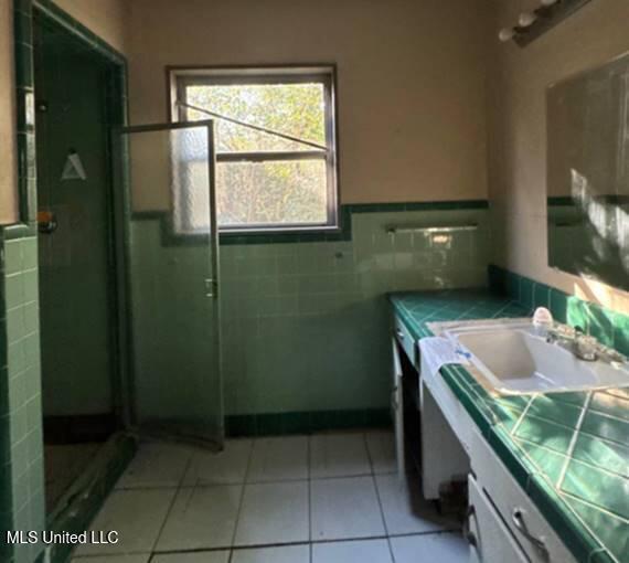 bathroom featuring tile patterned flooring, vanity, tile walls, and a shower with shower door