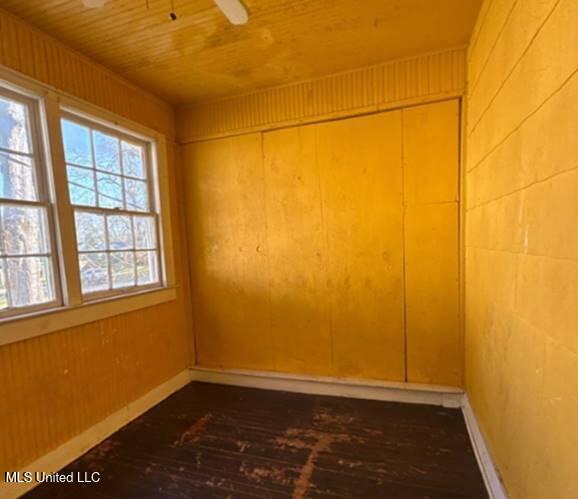 empty room with ceiling fan, wood ceiling, and wood walls