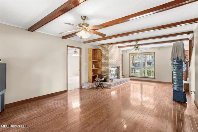 unfurnished living room featuring ceiling fan, hardwood / wood-style flooring, beamed ceiling, and a brick fireplace