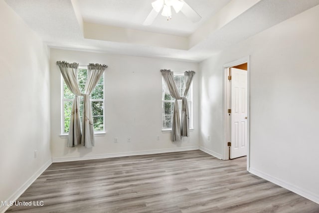 empty room with ceiling fan, a tray ceiling, and light hardwood / wood-style flooring