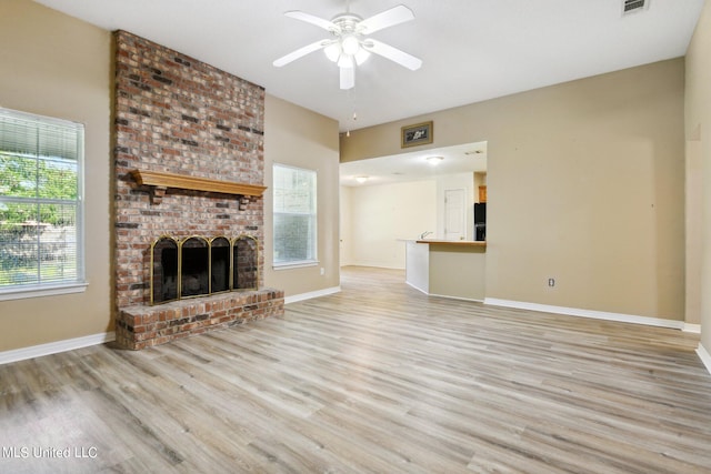 unfurnished living room with a brick fireplace, light wood-type flooring, and ceiling fan