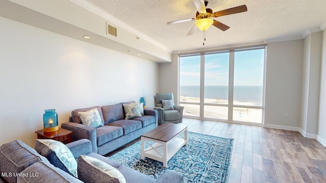 living room featuring floor to ceiling windows, ornamental molding, light wood-style floors, a ceiling fan, and a textured ceiling