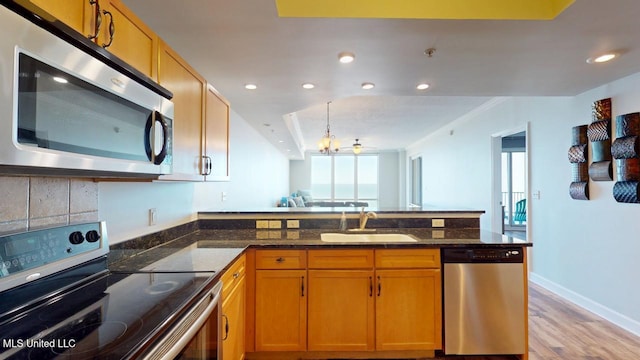 kitchen featuring appliances with stainless steel finishes, light wood-style floors, a sink, dark stone counters, and a peninsula