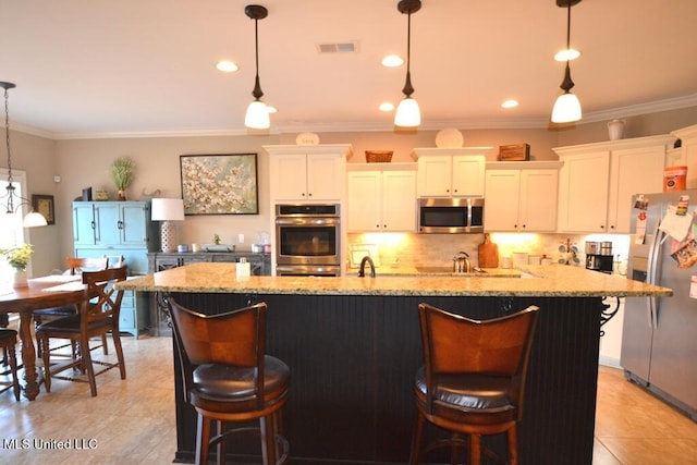 kitchen featuring hanging light fixtures, appliances with stainless steel finishes, a breakfast bar, and a large island with sink