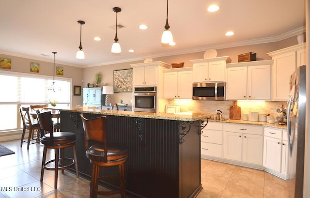 kitchen with an island with sink, appliances with stainless steel finishes, a breakfast bar area, decorative light fixtures, and white cabinetry