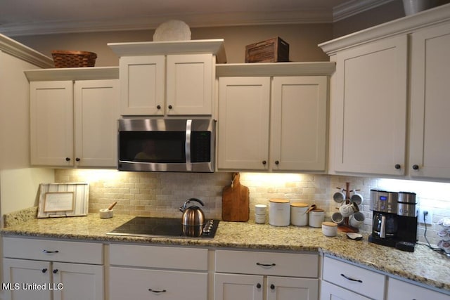 kitchen with tasteful backsplash, stainless steel microwave, crown molding, and white cabinetry