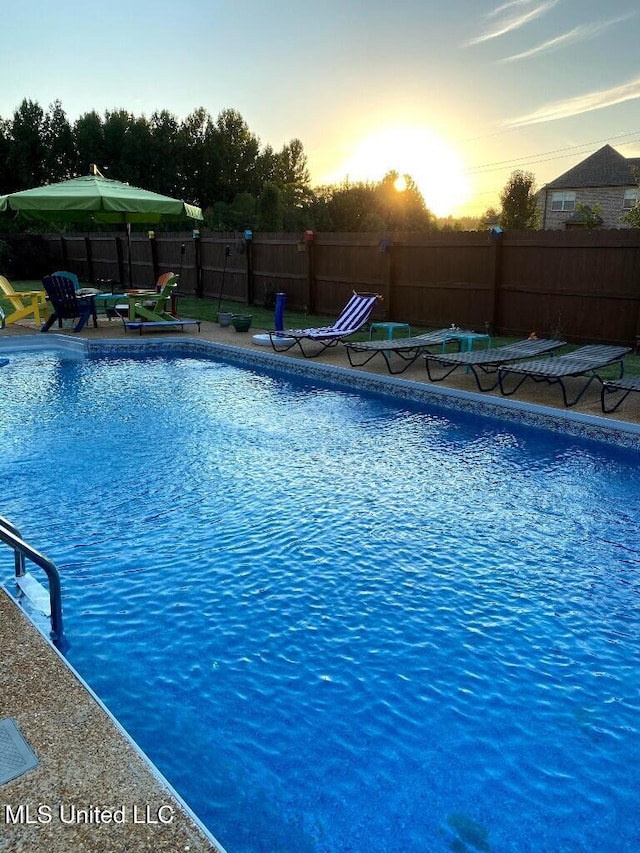 pool at dusk featuring a fenced in pool and a fenced backyard