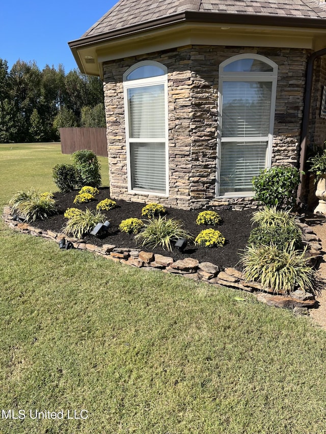 view of side of property featuring stone siding, a yard, and fence