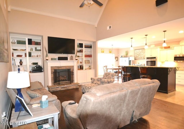 living room with light wood-style floors, a ceiling fan, crown molding, and a stone fireplace