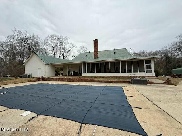 rear view of house featuring a chimney, a patio area, a sunroom, and a covered pool