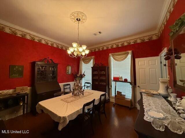 dining area with dark wood-style floors, crown molding, a notable chandelier, visible vents, and wallpapered walls