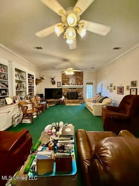 carpeted living area with ceiling fan, a fireplace, visible vents, and crown molding