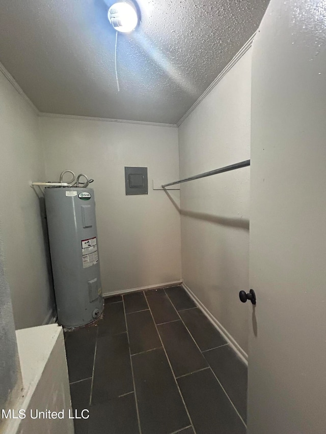 clothes washing area featuring electric water heater, a textured ceiling, dark tile patterned floors, and ornamental molding